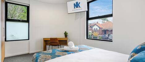 Una habitación de hotel con una cama, un escritorio y dos ventanas.