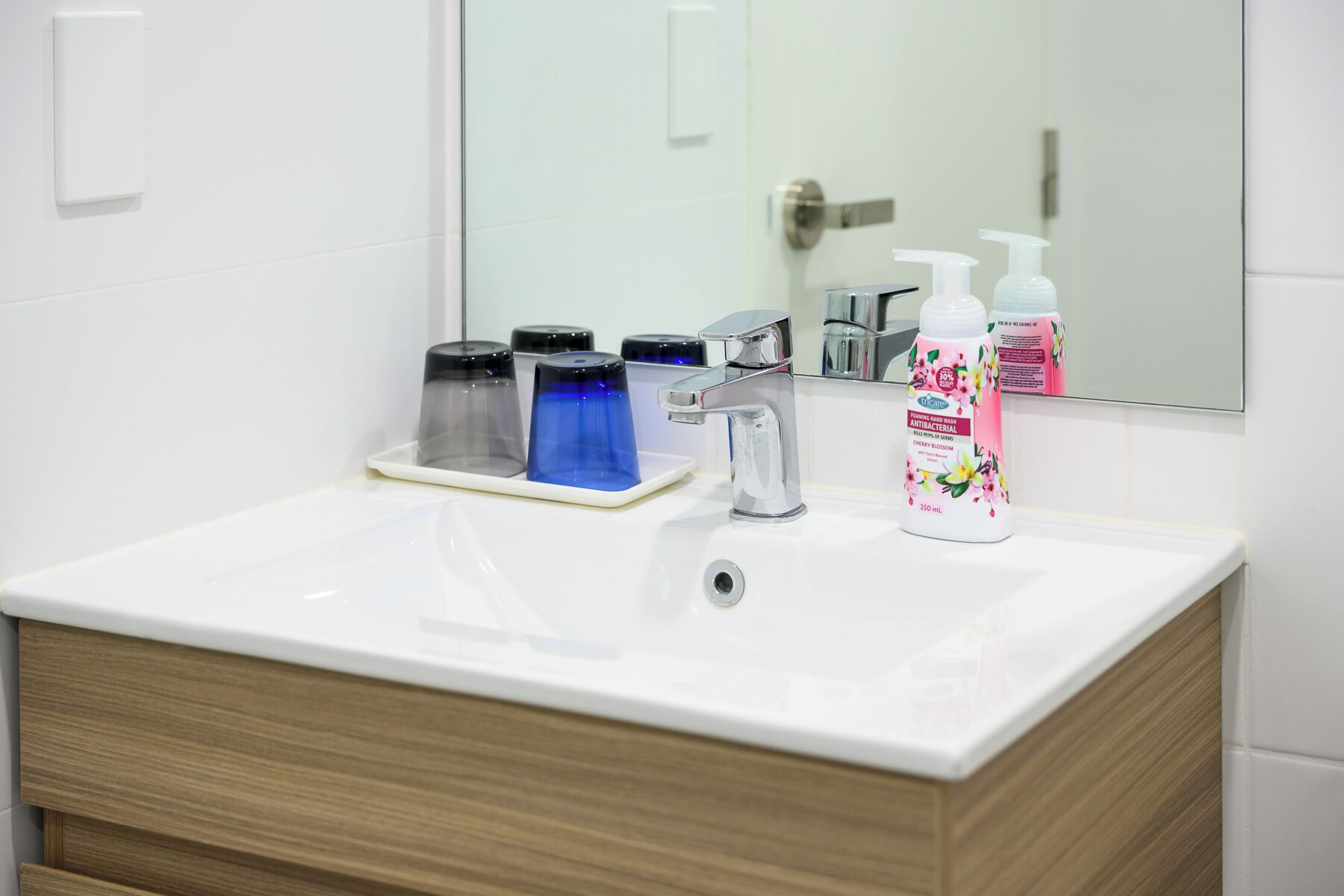 A bathroom with a white sink, a mirror, and a bottle of hand soap.