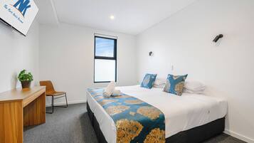 Une chambre d’hôtel avec un lit, un bureau, une chaise, une plante en pot et une fenêtre.