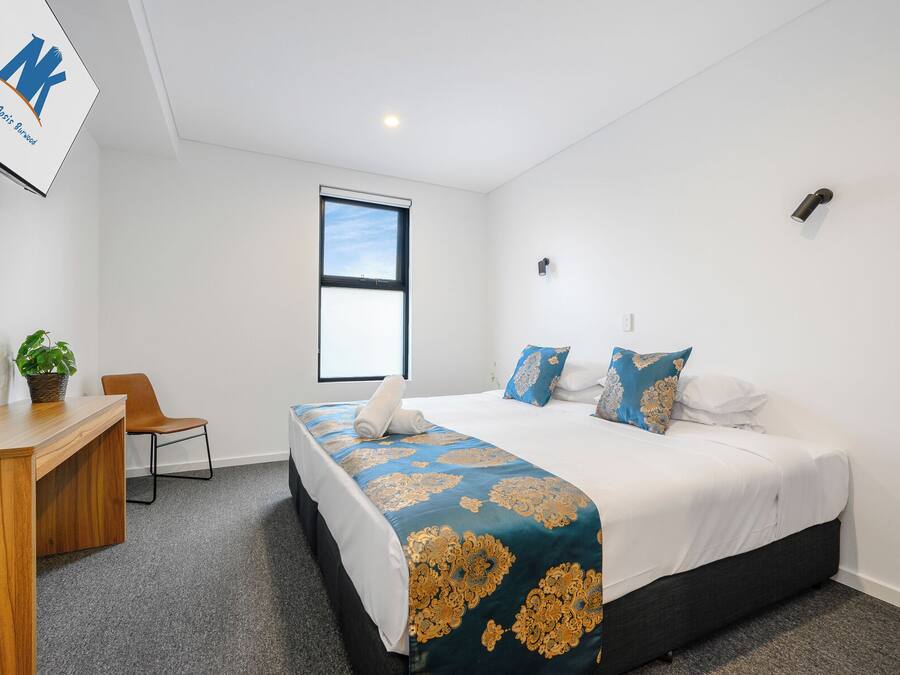 Une chambre d’hôtel avec un lit, un bureau, une chaise, une plante en pot et une fenêtre.