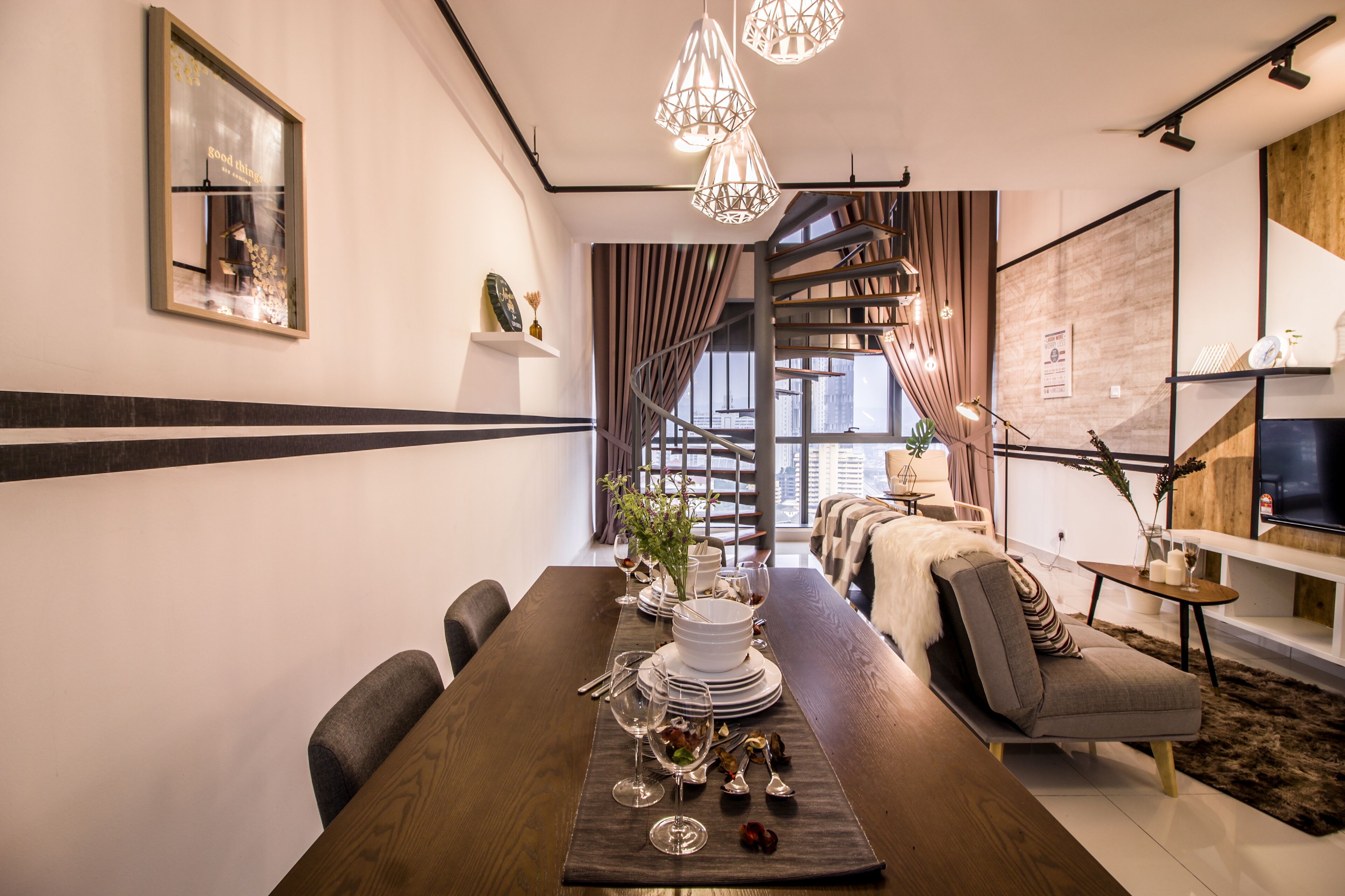 Un espace de repas moderne avec une longue table dressée pour un repas, un escalier menant à un niveau supérieur et un coin salon confortable avec un téléviseur.