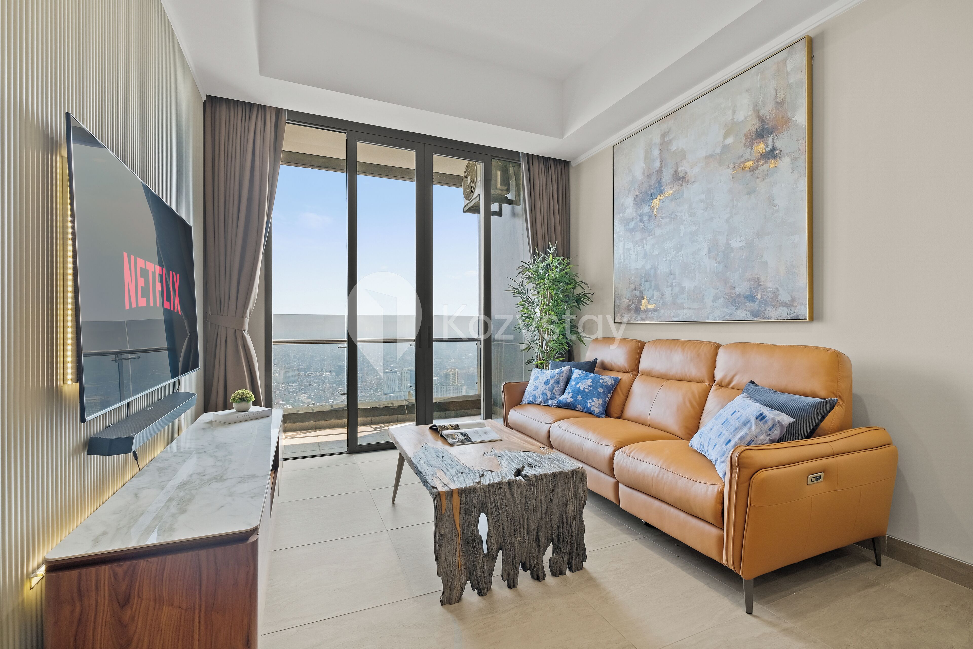 A modern living room with a large flat-screen TV, a wooden coffee table, a leather sofa with cushions, and a large abstract painting on the wall.