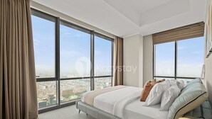 A modern bedroom with a large bed, a bedside table, and a view of a cityscape through large windows. - Terava by Kozystay - Kemayoran (Jakarta)