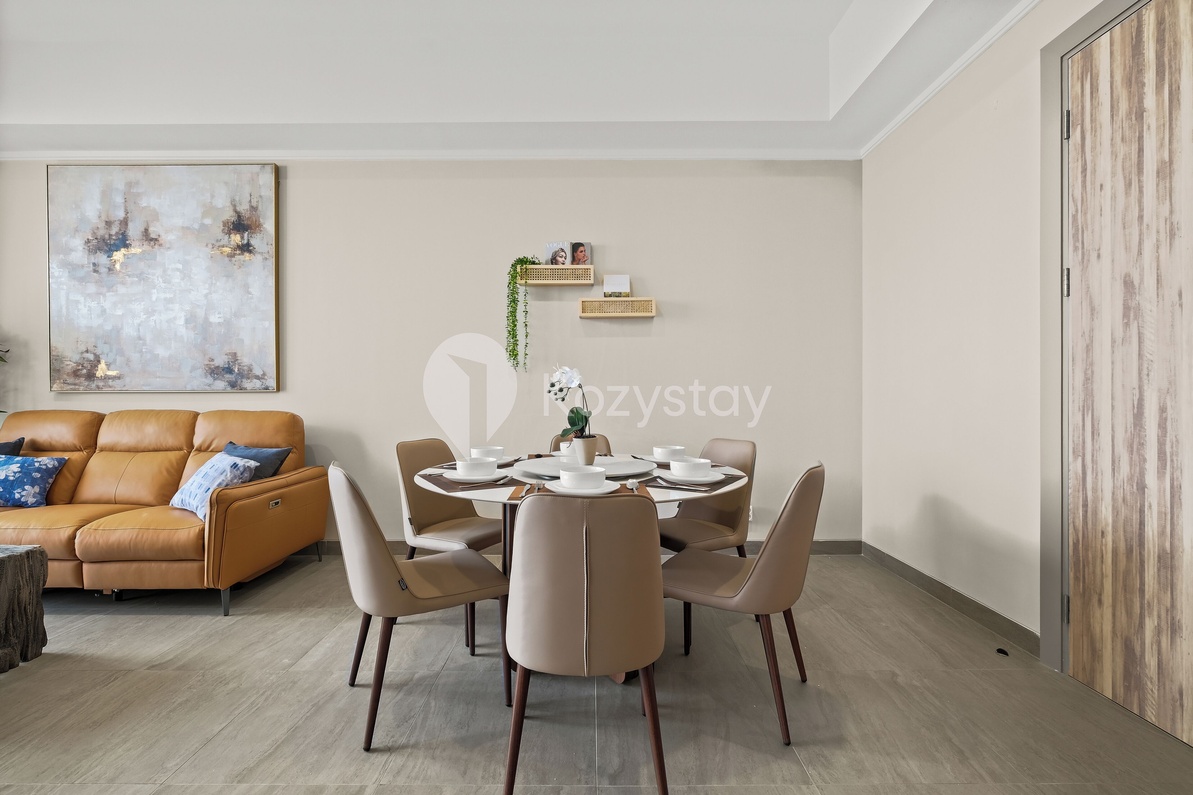 A modern living room with a round dining table, beige sofa, and a large abstract painting on the wall.