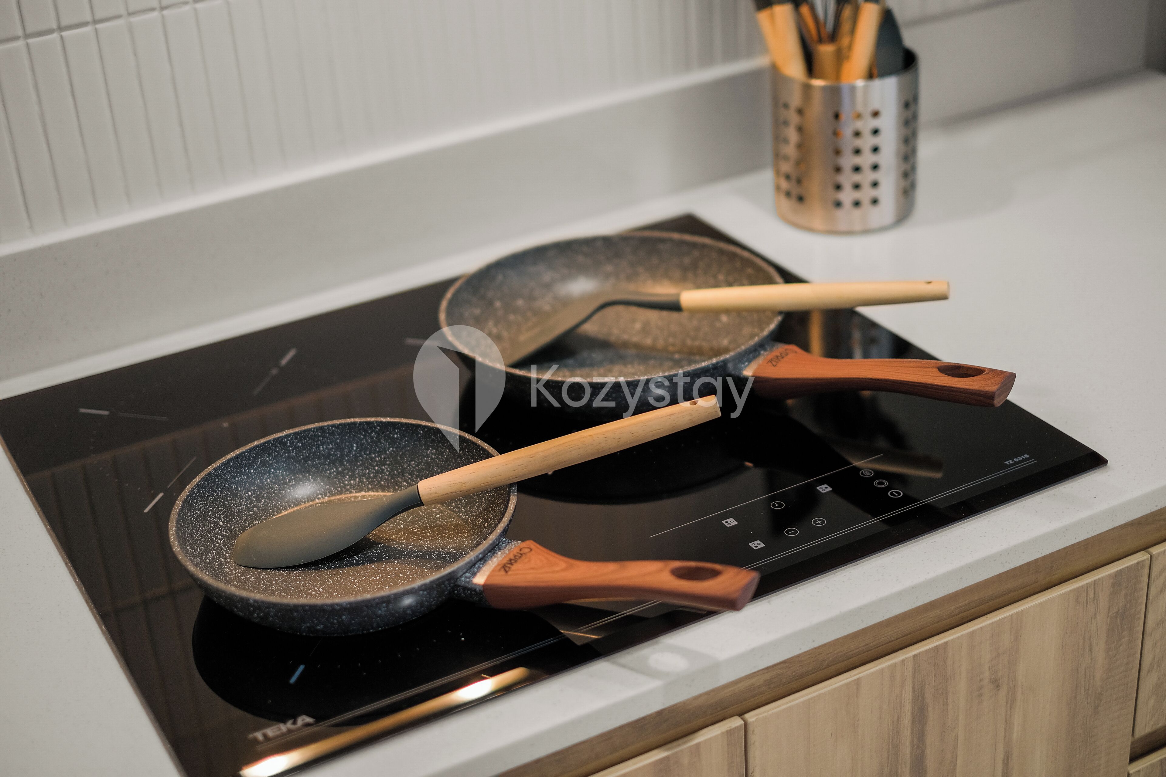 A kitchen with a black induction cooktop, a frying pan with wooden handles, and a utensil holder with wooden utensils.