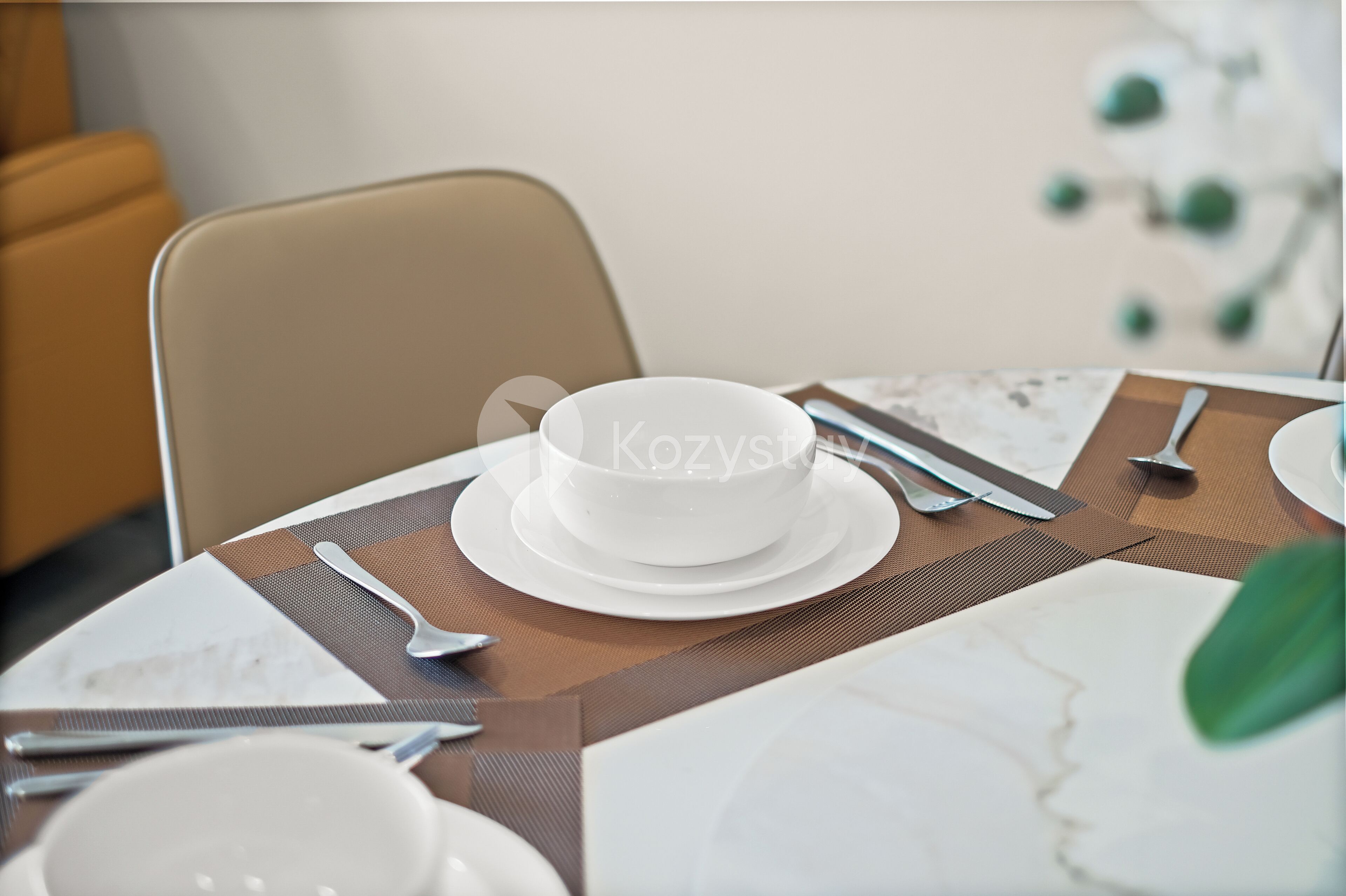 A dining table set with a white plate, a spoon, and a knife.