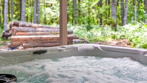 Een hottub met uitzicht op een bos en een stapel hout op de achtergrond.