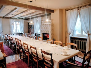 A dining area with a long table set for a meal, wooden chairs, a fireplace, and a view of the outdoors.
