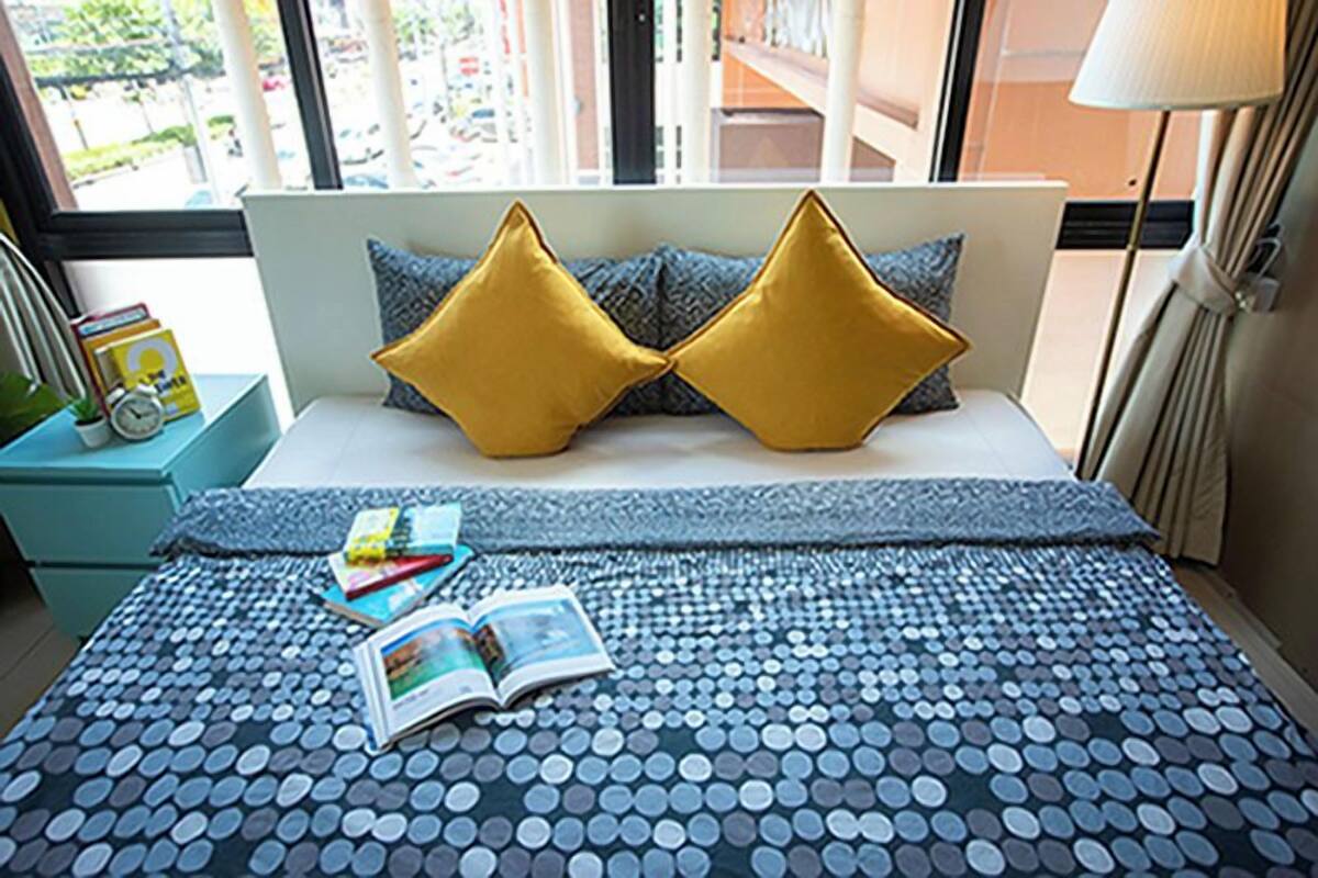 A neatly made bed with a blue and white polka dot bedspread, two gold pillows, and a book on the bed.