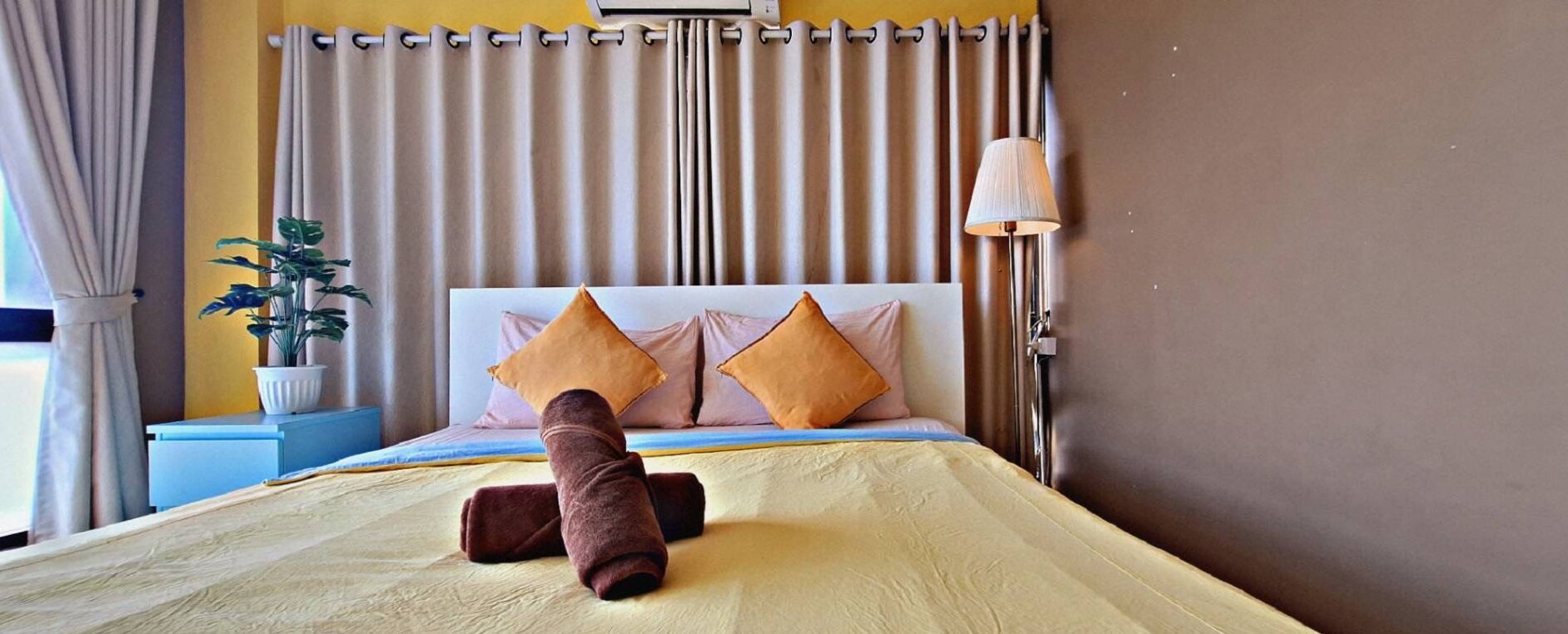 A neatly made bed with two pillows, a bedside lamp, and a plant on a bedside table.