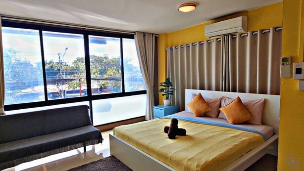 A hotel room with a large window, a bed with pillows, a bench, and an air conditioning unit. - Peony's Home (Bangkok)