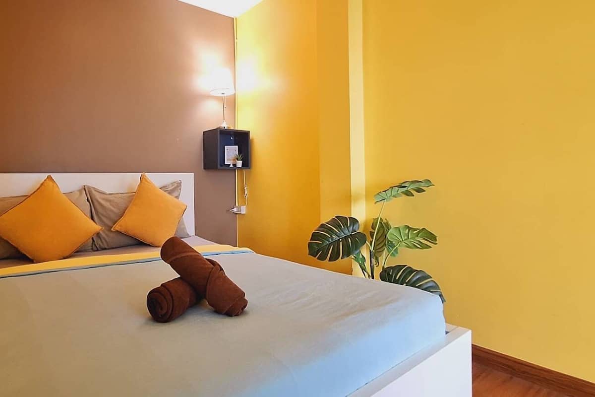 A hotel room with a bed, pillows, a bedside lamp, and a potted plant.