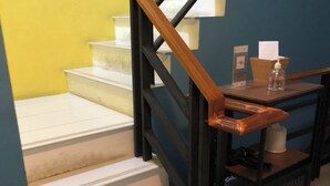 A staircase with wooden handrails and white steps, leading to a landing area with a small table and a tissue box. - Peony's Home (Bangkok)
