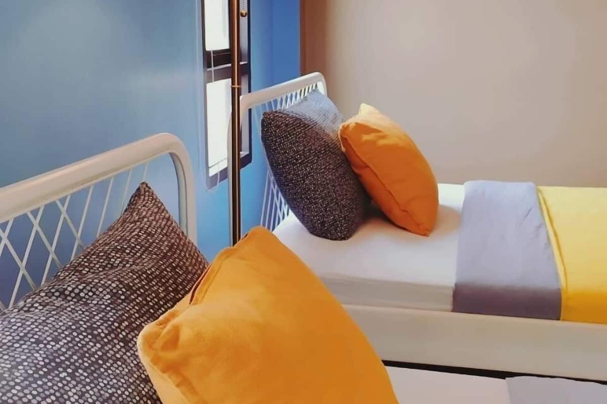 A bed with a white metal frame, a blue wall, and a floor lamp with a white lampshade.