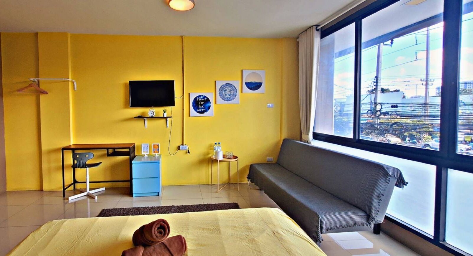 A hotel room with a large window, a bed, a desk, a TV, and a sofa.