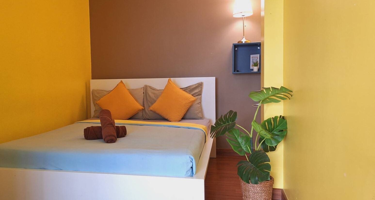 A bed with a headboard, two pillows, a blanket, and a brown towel. There is a potted plant to the right.