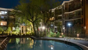 Piscina à noite, rodeada por árvores e edifícios.