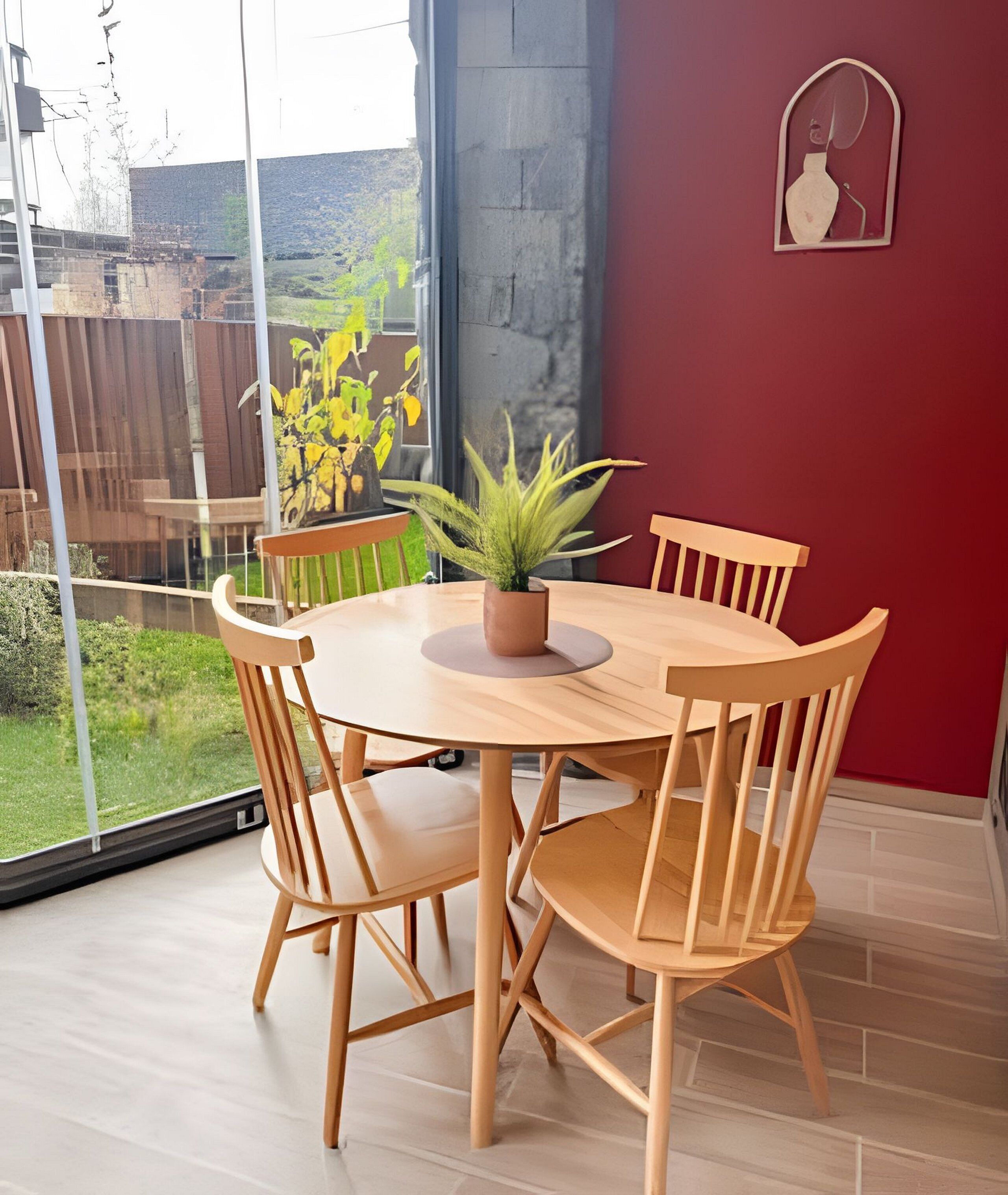 Un coin repas avec une table ronde en bois et des chaises, une plante en pot et un mur rouge.