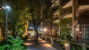 Uma passarela noturna ladeada por árvores e edifícios modernos com fachadas de vidro.