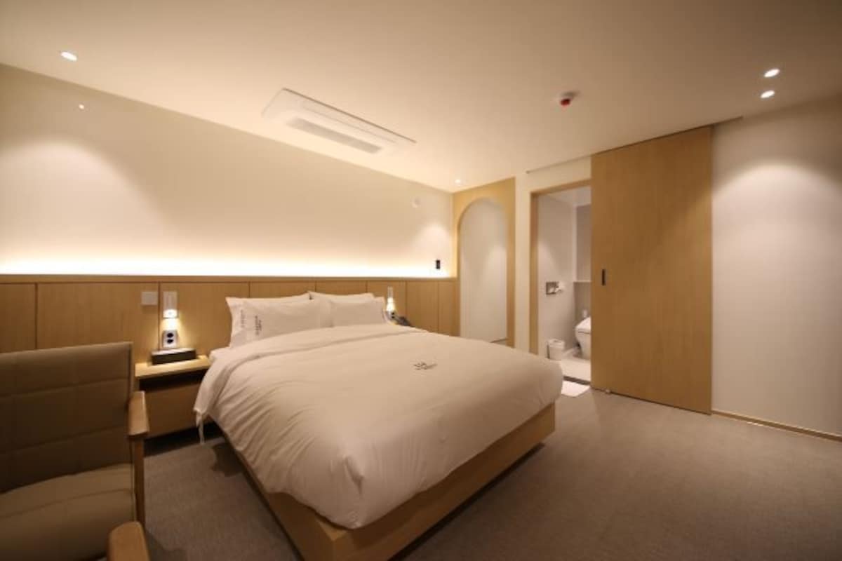 Una habitación de hotel moderna con una cama grande, mesitas de noche, una silla y un vestidor.