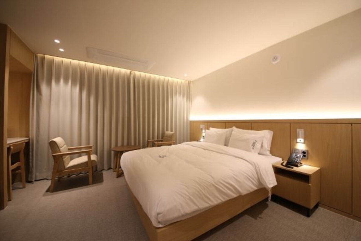 Una habitación de hotel con una cama grande, una mesita de noche con lámpara, una silla y un escritorio.