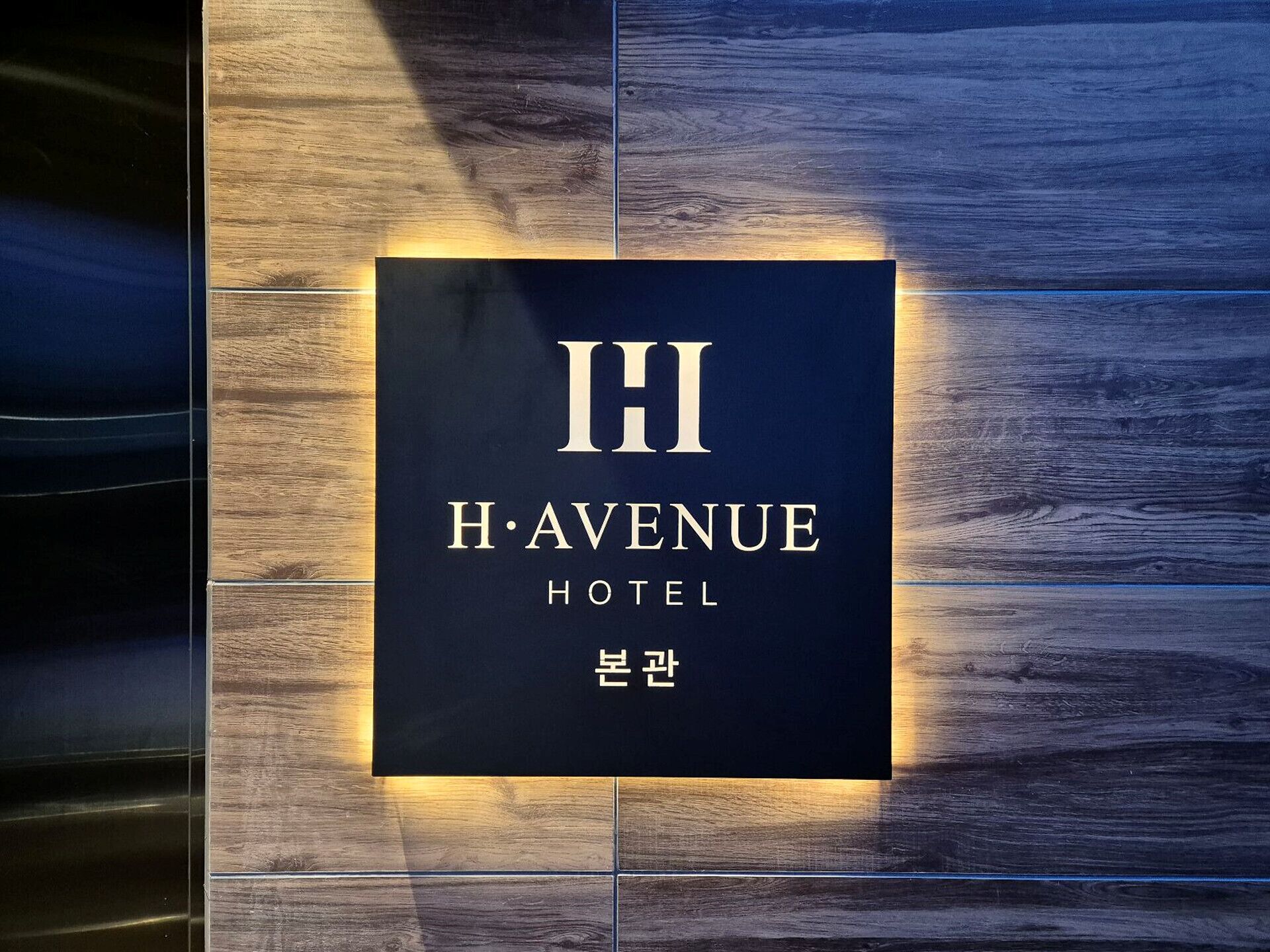 A sign for H. Avenue Hotel with a minimalist design and a wooden background.