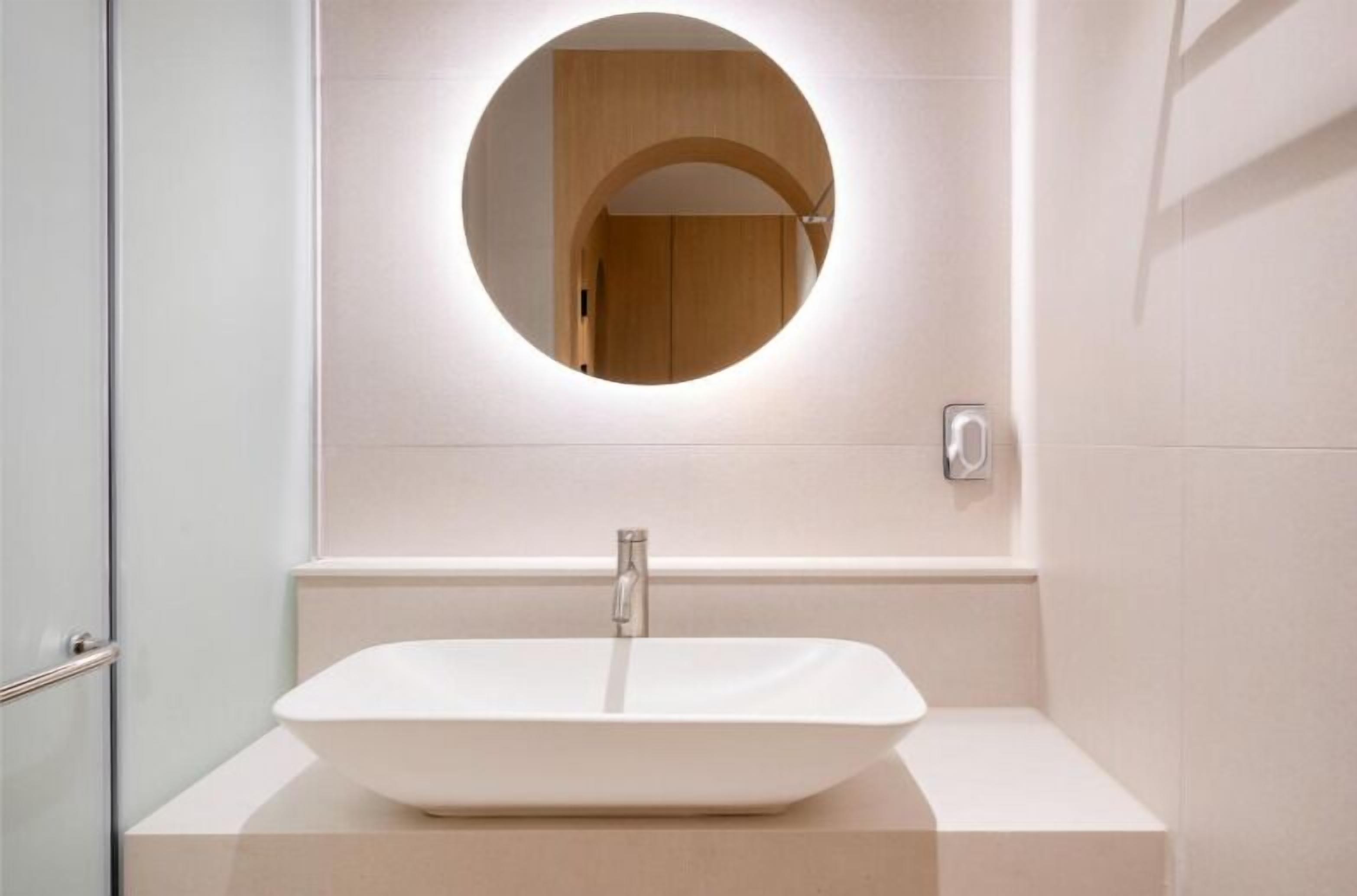 Une salle de bain avec un lavabo blanc, un miroir rond et un meuble-lavabo en bois.