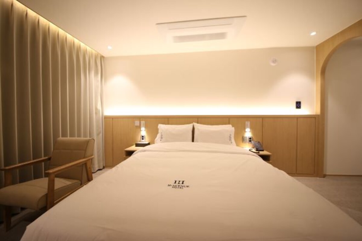 Habitación de hotel con una cama grande, dos mesitas de noche con lámparas, una silla y un cabecero de madera.