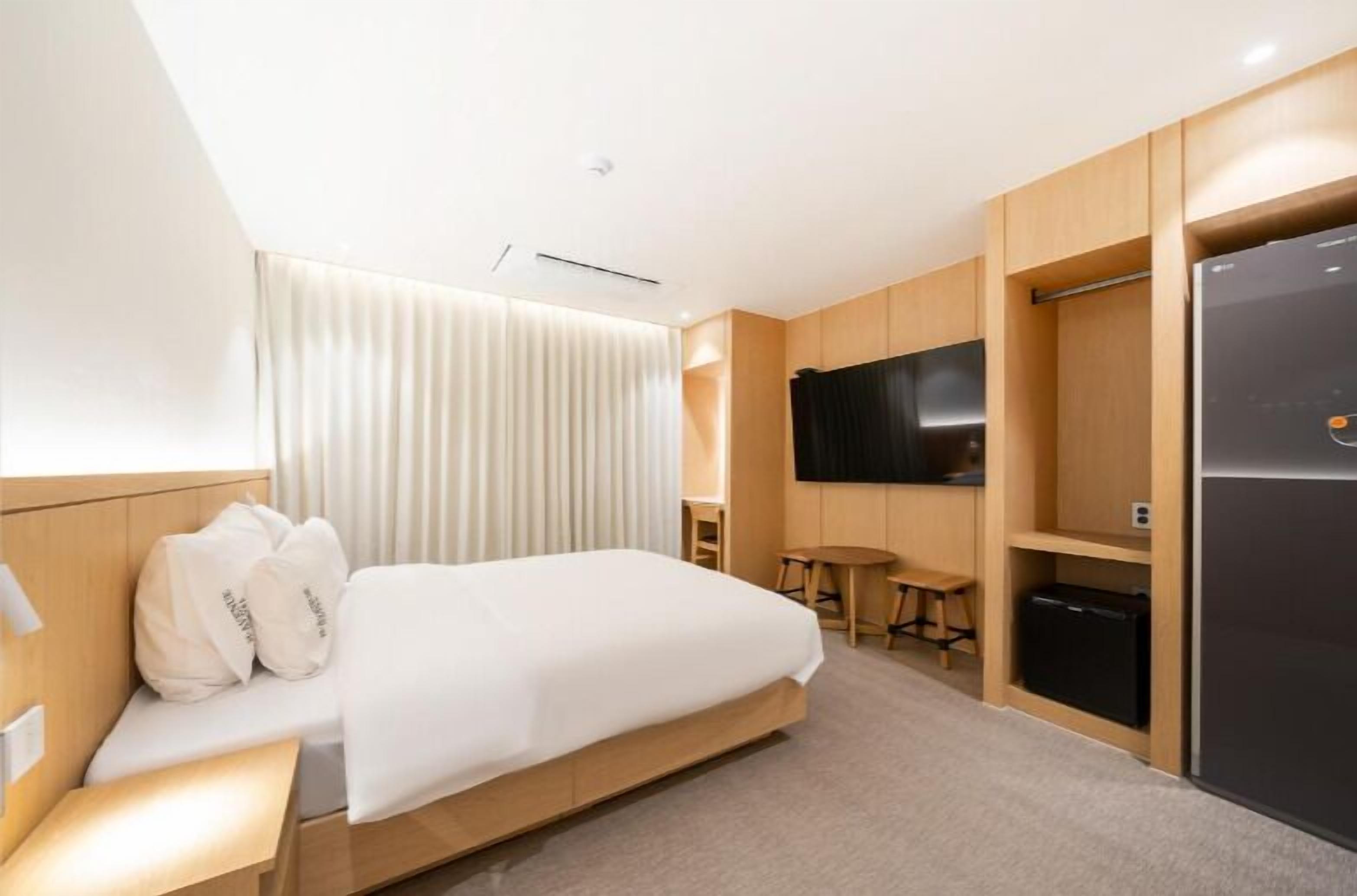 Une chambre d’hôtel moderne équipée d’un lit, d’un téléviseur à écran plat, d’un réfrigérateur et d’une petite table avec des tabourets.