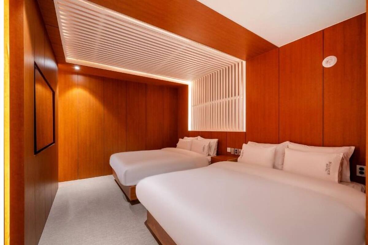 A hotel room with two beds, wooden paneling, and a modern ceiling design.
