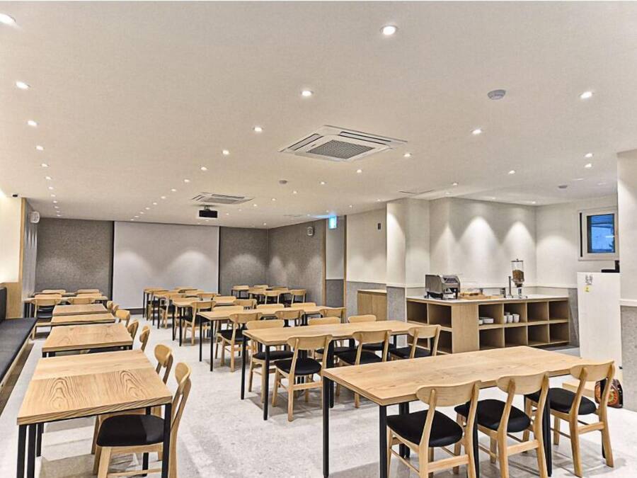 Una sala de conferencias moderna con varias mesas y sillas de madera, equipada con un proyector y una máquina de café.