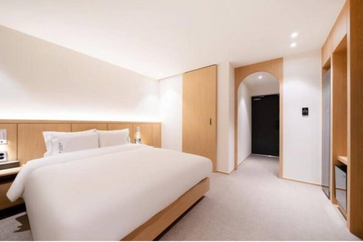 A modern hotel room with a large bed, wooden headboard, and a minimalist design.