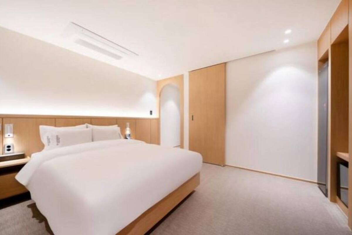 A modern hotel room with a large bed, wooden headboard, and a built-in wardrobe.