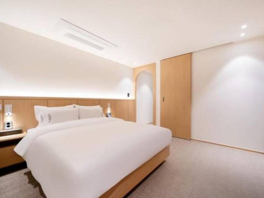 A modern hotel room with a large bed, wooden headboard, and a built-in wardrobe.