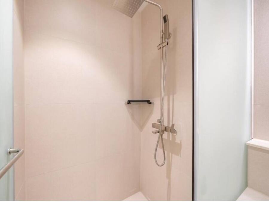 A small, enclosed shower area with a handheld showerhead and a handheld faucet.