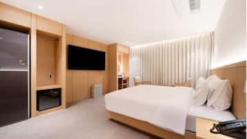 A modern hotel room with a large bed, a flat-screen TV mounted on the wall, a desk with a chair, and a built-in wardrobe.