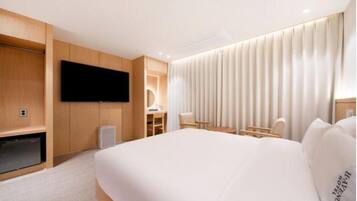 Habitación de hotel con una cama grande, un televisor de pantalla plana montado en la pared, un escritorio con una silla y una ventana con cortinas.