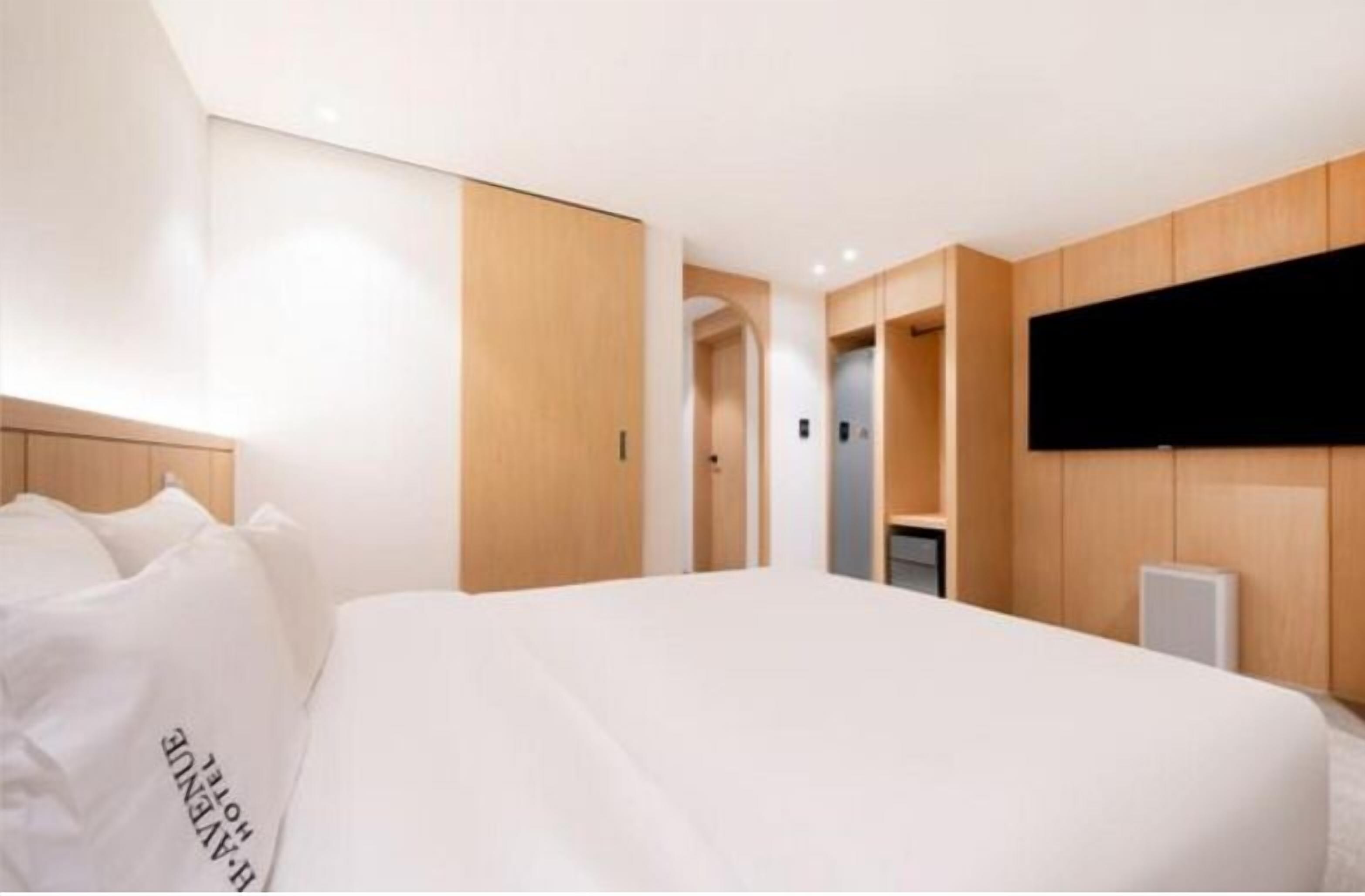 Une chambre d’hôtel moderne dotée d’un grand lit, de lambris en bois, d’un téléviseur à écran plat fixé au mur et d’un couloir menant à d’autres chambres.