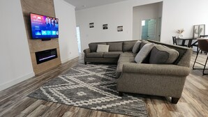 Een moderne woonkamer met een hoekbank, een flatscreen-tv aan de muur, een open haard en een kamerkleed met een patroon.