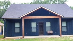 Een twee verdiepingen tellend huis met een donkerblauwe gevel, een puntig dak en een veranda met twee stoelen.