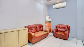 A room with two leather sofas, a wooden cabinet, and a vertical banner. - Hotel O Tegal near near Pacific Mall Tegal formerly Hugo Suites Family (Tegal)