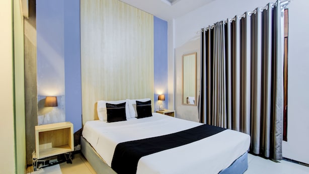 A hotel room with a large bed, bedside tables, a mirror, and a curtain. - Hotel O Tegal near near Pacific Mall Tegal formerly Hugo Suites Family (Tegal)