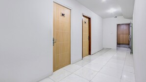 A hallway with two wooden doors, white tiled flooring, and a ceiling light. - Hotel O Tegal near near Pacific Mall Tegal formerly Hugo Suites Family (Tegal)
