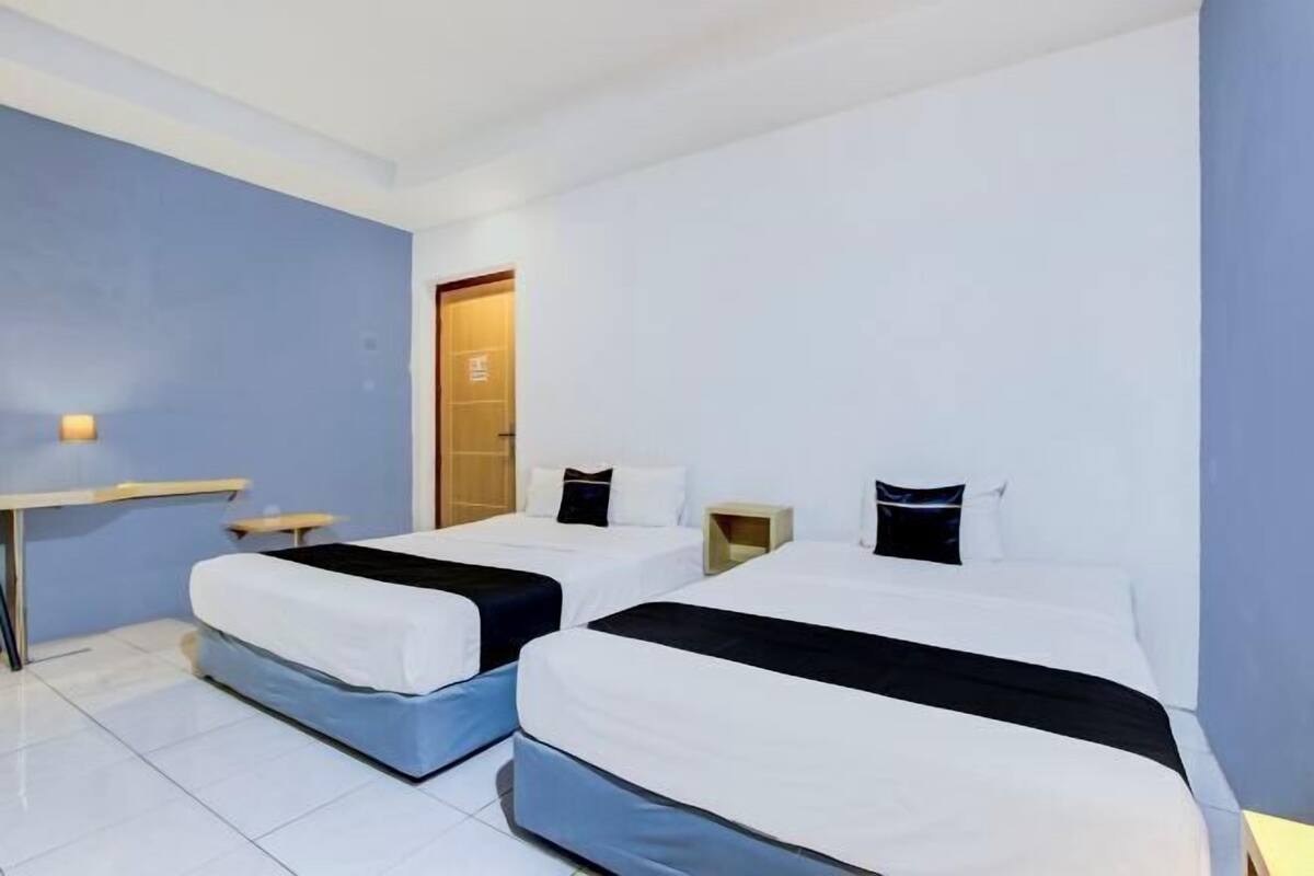 A hotel room with two beds, a desk, and a door.