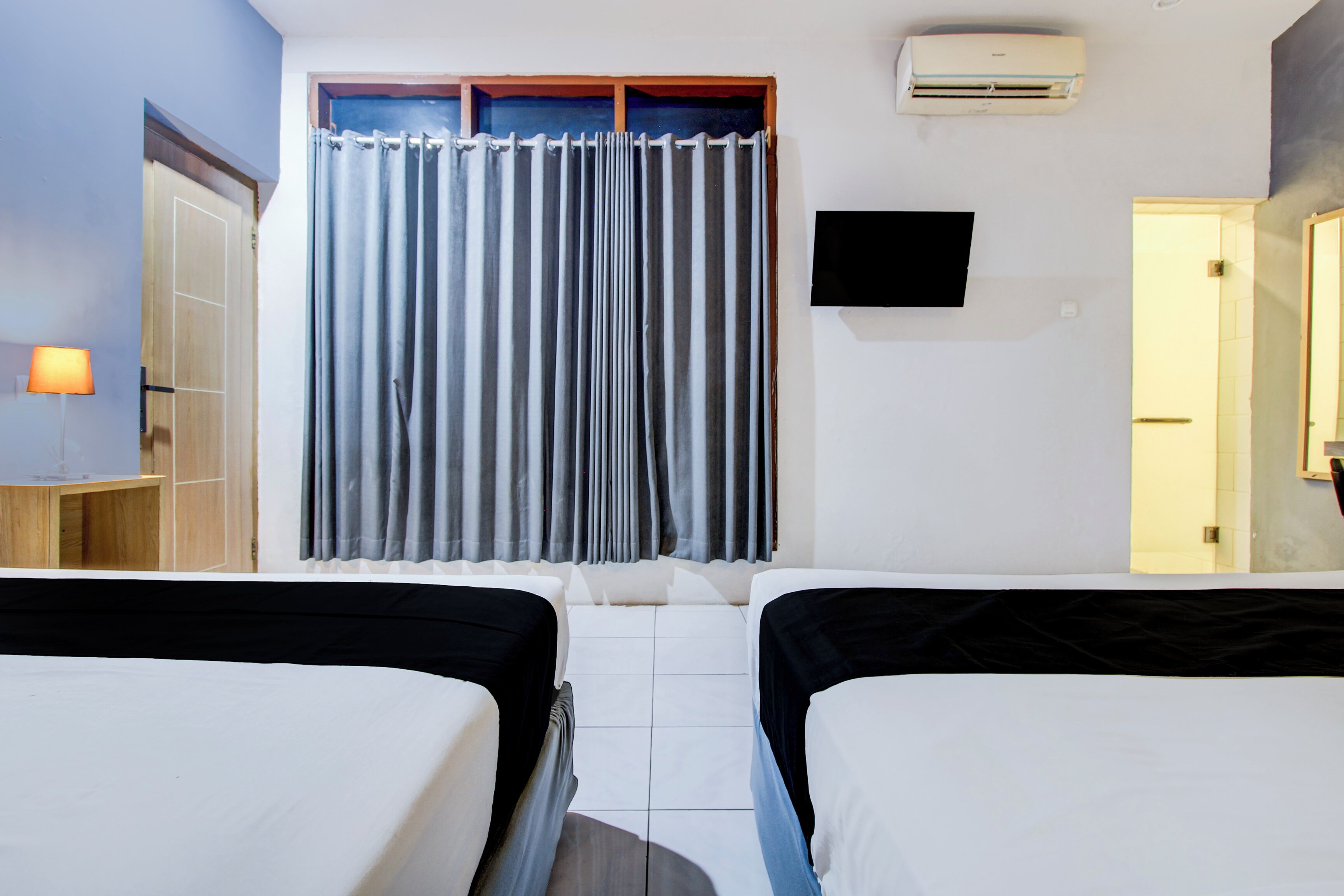 A hotel room with two beds, a TV, an air conditioner, and a curtain.