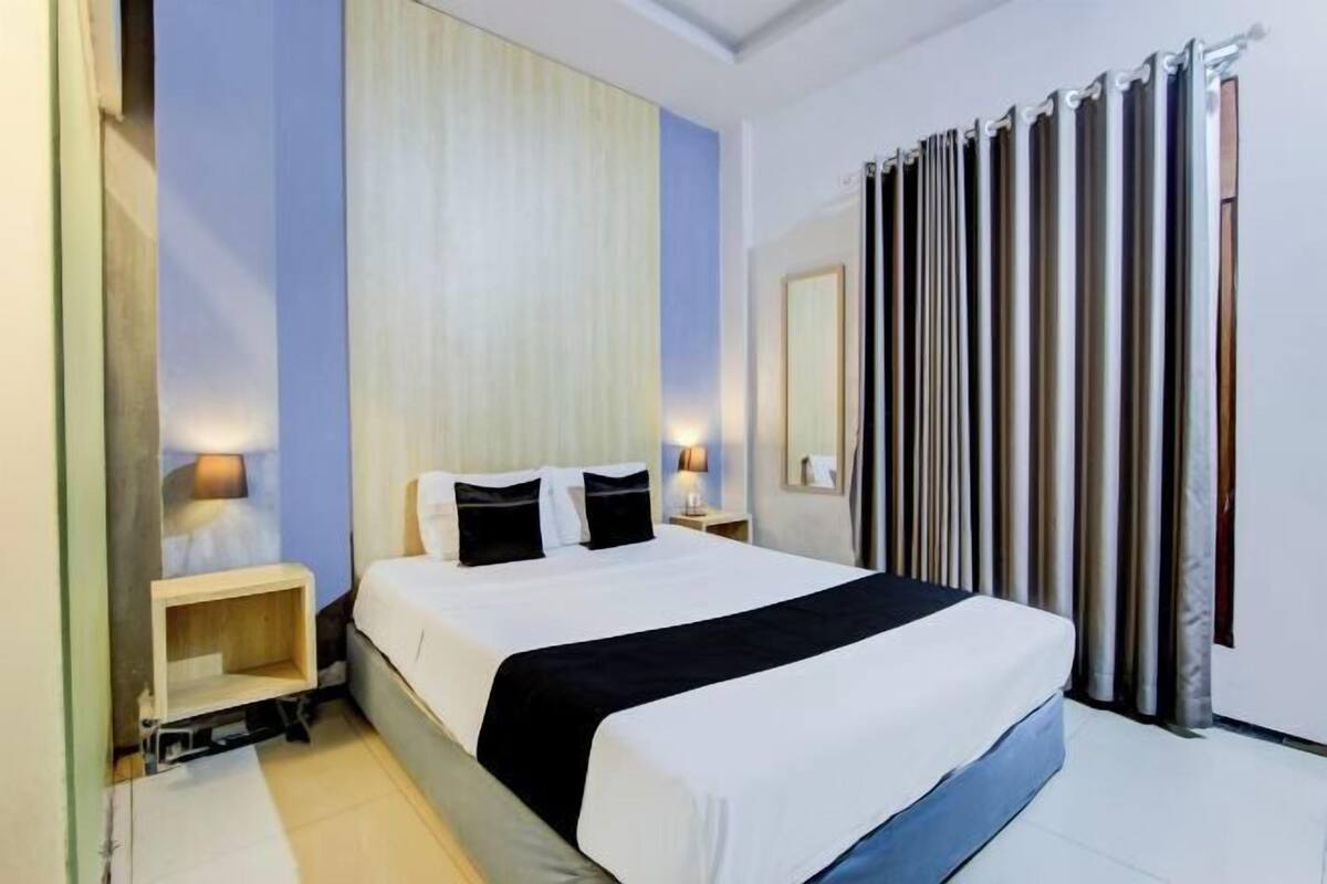 A hotel room with a bed, bedside tables, a mirror, and a curtain.