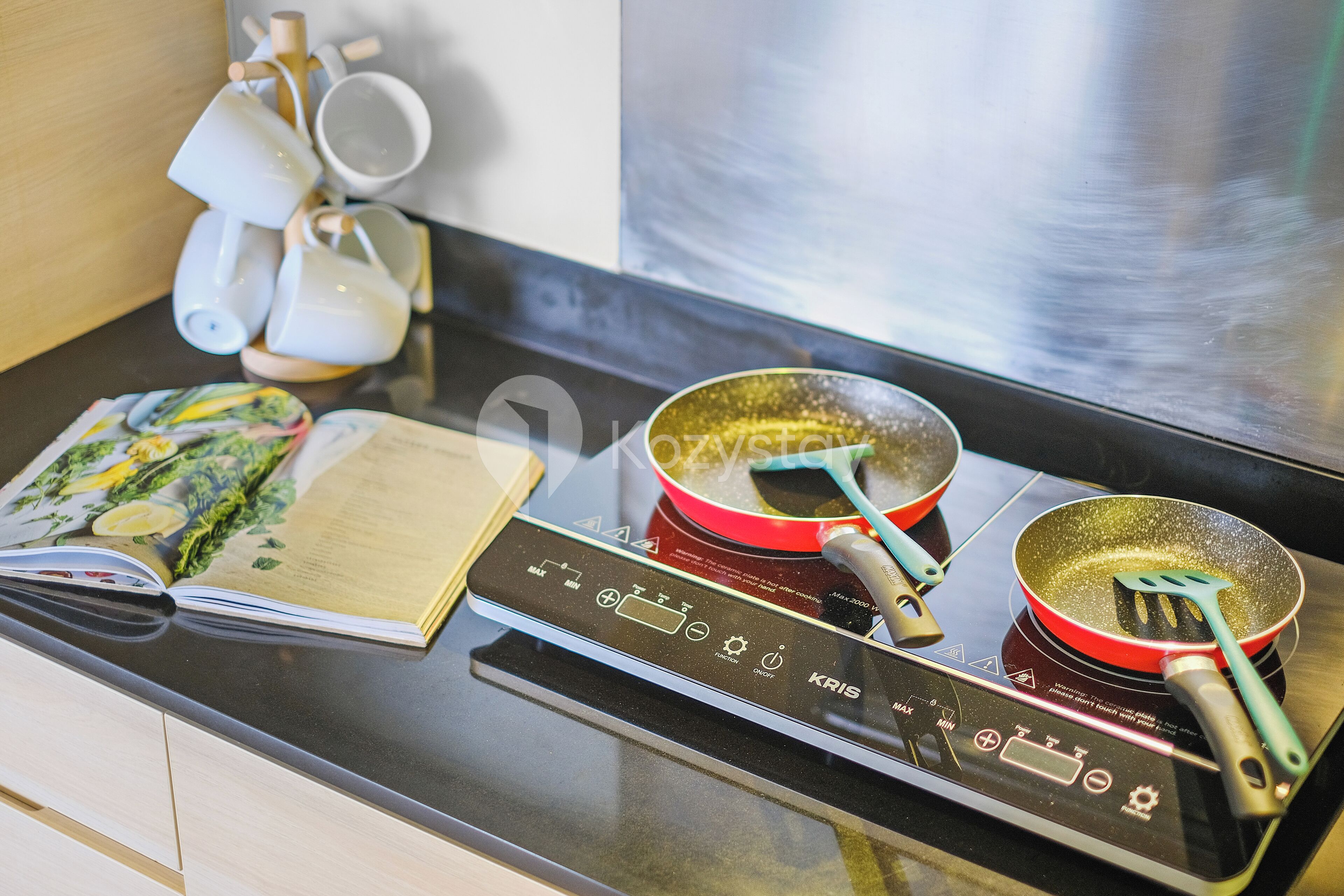 A kitchen with a modern induction cooktop, a red frying pan, and a cookbook on the counter.