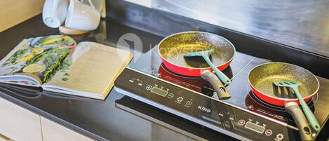 A kitchen with a modern induction cooktop, a red frying pan, and a cookbook on the counter.