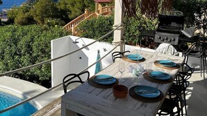 Zona pranzo all'aperto con tavolo apparecchiato per quattro, affacciata su una vista panoramica del mare e del verde.
