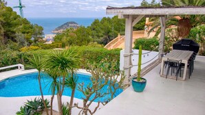 Una piscina con vista sul mare, circondata da piante tropicali e un'area barbecue.
